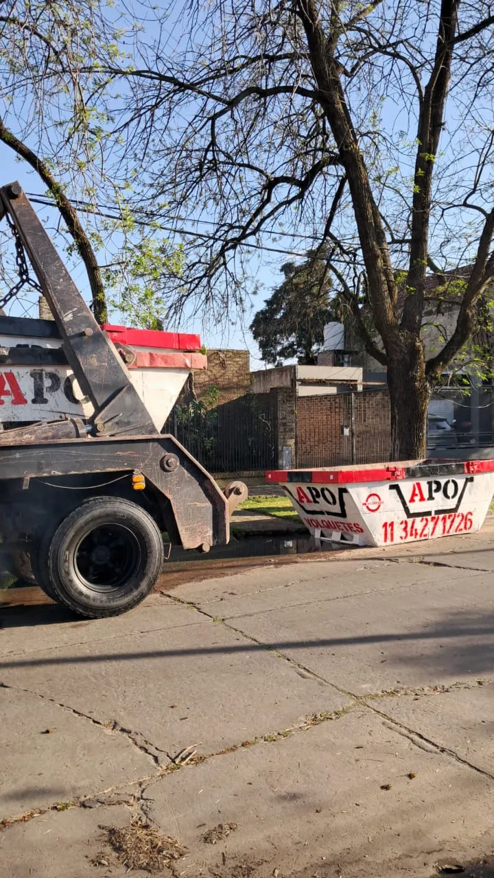 Camión de APO con brazo hidráulico bajando un volquete en la calle